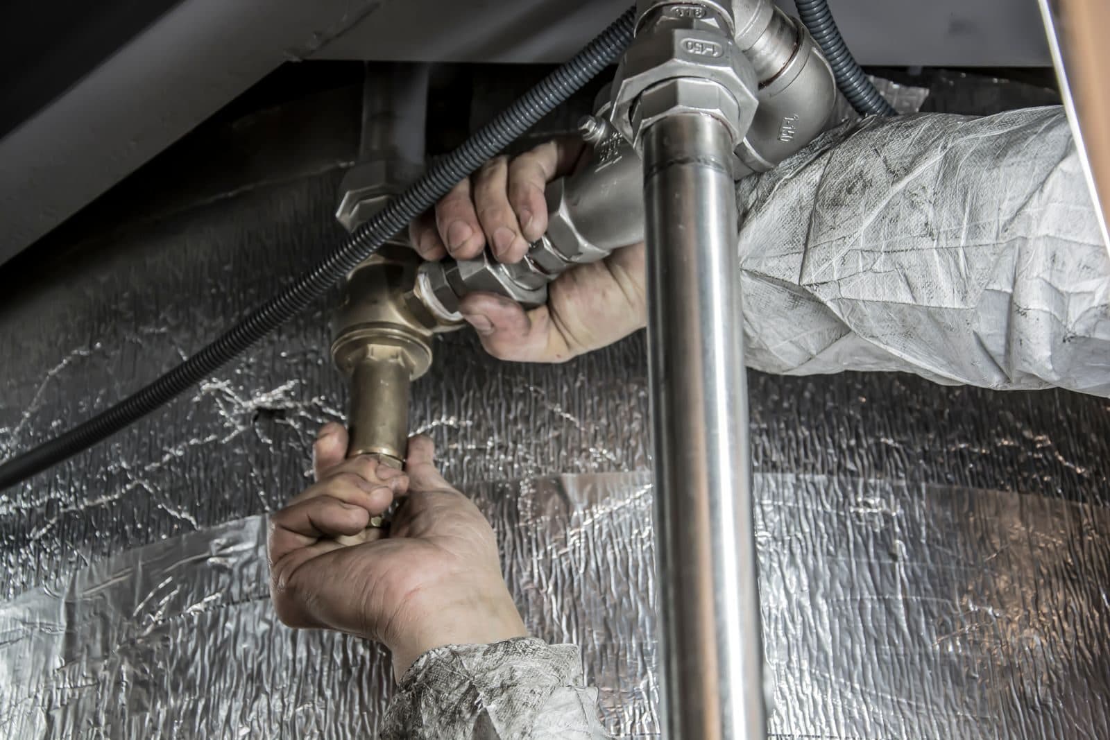 Hands threading a brass fitting onto a copper pipe