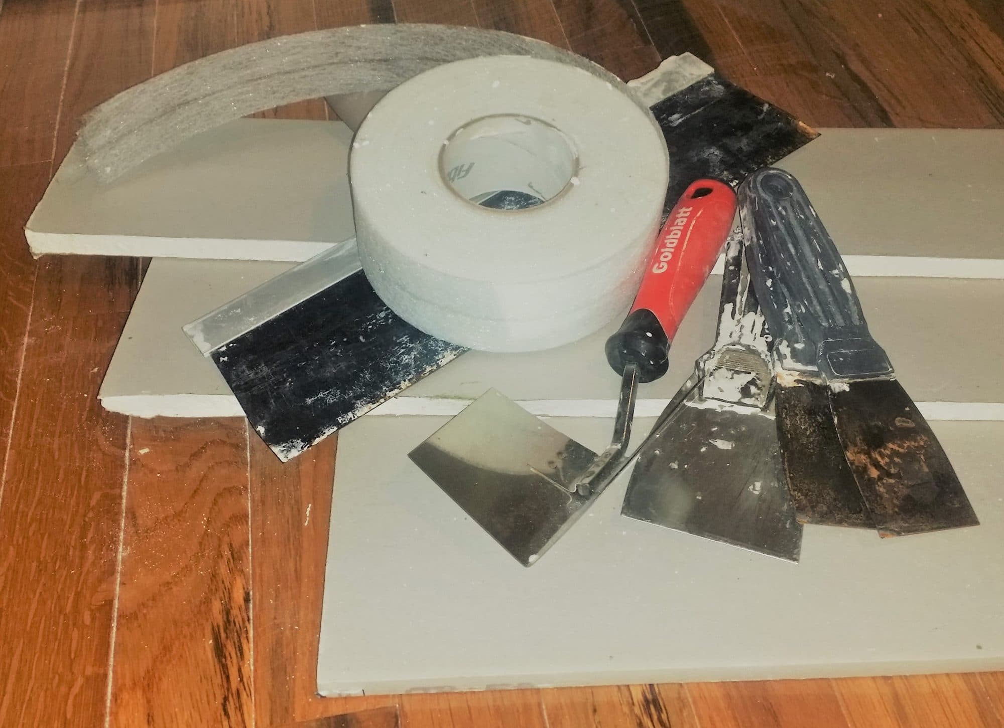 Drywall tape, mud pan, and knives on a board